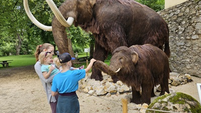 Drei Kinder streicheln ein Baby-Mammut im MAMUZ Asparn/Zaya.