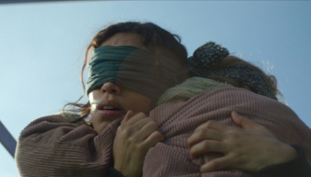 Ein Standbild aus dem Film Bird Box: Barcelona. Eine Frau trägt eine Augenbinde und trägt ein kleines Mädchen in ihren Armen.