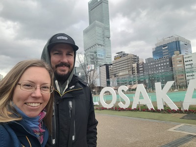 Paar vor Osaka Schriftzug, im Hintergrund ein Hochhaus