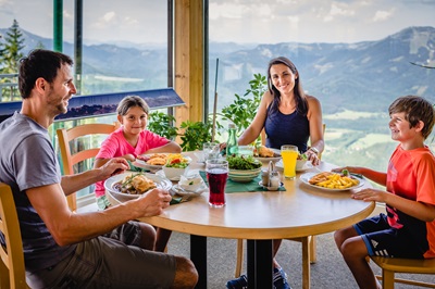 Familie mit Mann, Frau, Sohn und Tochter beim Berggasthof auf der Bürgeralpe beim Essen mit Schnitzel und Pommes, diversen Hauptspeisen und Getränken.