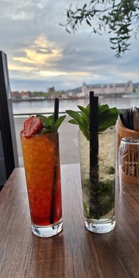 Zwei Cocktails stehen auf einem Tisch, dahinter der Hafen von Oslo.