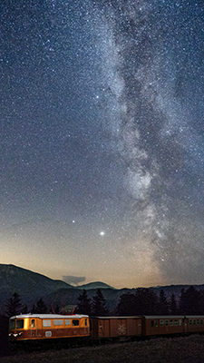 Ötscherbär fährt durchs Bild, im Hintergrund ein leuchtender Sternenhimmel
