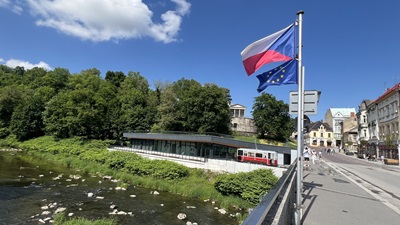 Brücke auf der Olga, die den tschechischen Teil von Teschen mit dem polnischen verbindet. Zu sehen ist die Flagge von Tschechien und der EU, das Flussufer und ein roter Waggon der alten Tramway.