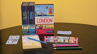 Die Boxen von Next Station London, Paris und Tokyo. Davor ist das Spielmaterial der London Version am Tisch ausgebreitet