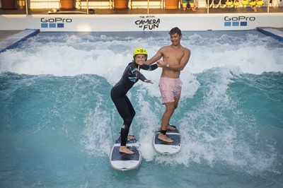 Mann stützt junge Frau beim Surfen auf der stehende CityWave. Beide lächeln.