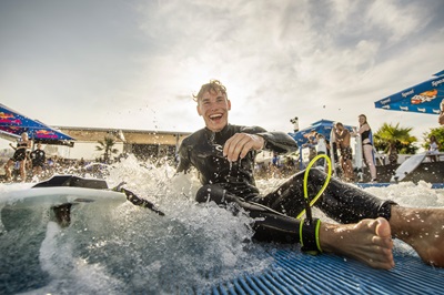 Junger blonder Mann im Neoprenanzug lacht am Beckenrand der CityWave im Multiplex Wiener Neudorf.