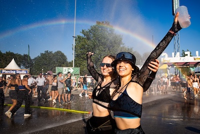 Zwei Frauen stehen arm in Arm am Frequency Gelände unter einem Regenbogen