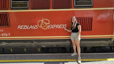 Frau steht vor der roten Lok des Reblaus Express und zeigt auf das Logo