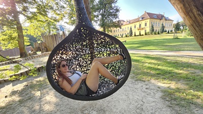 Frau in Hängesessel im Schlosspark mit Schloss Eckartsau im Hintergrund.