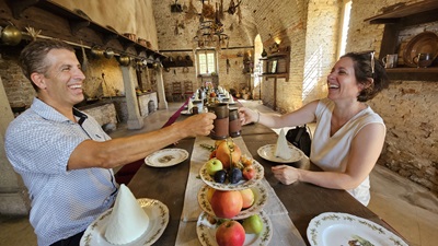 Mann und Frau stoßen in der Wildküche beim Schloss Niederweiden bei Tisch mit Krügen an und lachen.