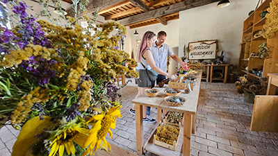 Getrocknete Blumen, im Hintergrund Miriam und Christian, die sich getrocknete Kräuter ansehen