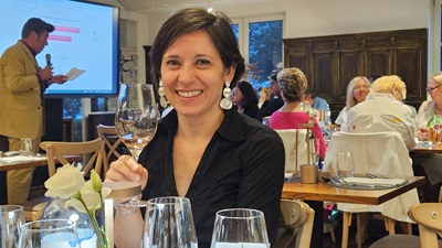 Frau mit Wein in der Hand, dahinter Mat Schuh mit Votingergebnis und weitere Gäste beim Wine Battle im Handwerk Restaurant am Wiener Gürtel.