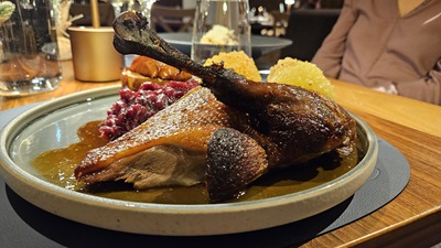 Viertel einer gebratenen Weidegans am Teller im Handwerk Restaurant mit Rotkraut, Erdäpfelknödel, Bratapfel und Saft.