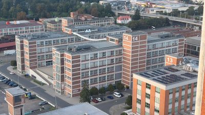 Mehrere Fabriksgebäude, in Modulbauweise errichtet. Mit Backstein, Stahlträgern und großen Glasfenstern.