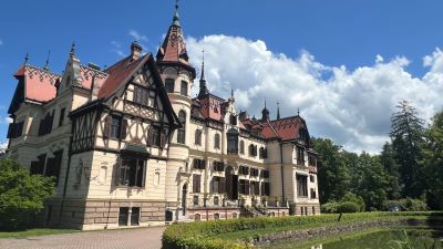 Schloss Leschna in einem Schlosspark. Die Fassade spielerisch mit vielen Türmchen und Zinnen gestaltet. Fachwerk und verschiedenfarbig gestaltete Ziegeldächer erwecken den Eindruck eines kleinen Märchenschlosses.