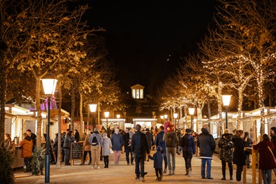 Menschen schlendern neben Laterne durch eine Allee mit Weihnachtsstanderln beim Advent im Park in Baden