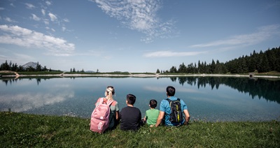 Familie mit Mann, Frau und zwei Kindern sitzt beim Speichersee am Annaberg in der Wiese und blickt auf das Wasser.