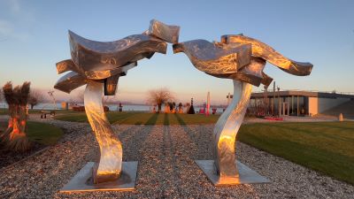 Eine monumentale Stahlplastik in der Form eines Tors. Der Edelstahl leuchtet im Abendrot.