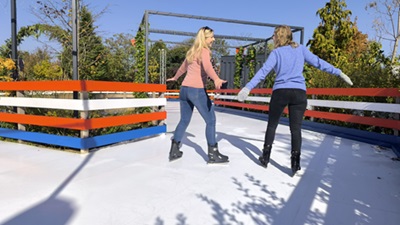 Zwei Frauen laufen in der Sonne im Kittenberger Eiszaubergarten auf Kunsteislaufplatten, die aussehen wie echtes Eis.