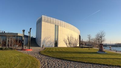 Das moderne Gebäude des Danubiana Museums, ein weißer Bau in Form einer Ellipse. Das Gebäude steht an einer grünen Wiese, am Rand einer Wasserfläche.