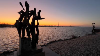 Moderene Plastiken, stilisierte Menschen am Ufer einer Wasserfläche im Abendrot. 