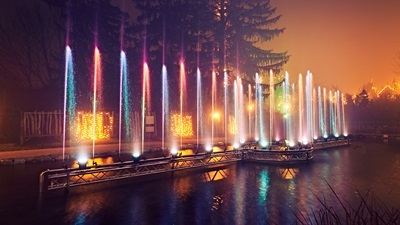 Der Flossteich in den Kittenberger Erlebnisgärten bei Nacht. Die Wasserstrahlen des Brunnens werden bunt mit Scheinwerfern beleuchtet.