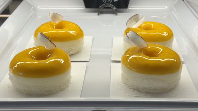 Vier gelb-weiße Patisserien in Ringform auf weißem Porzellan.