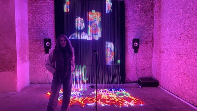 eine Frau steht vor einer beleuchteten Wand und einen Vorhang mit Lichtinstallationen vor dem Werk enter bei der khroma Ausstellung in Wien