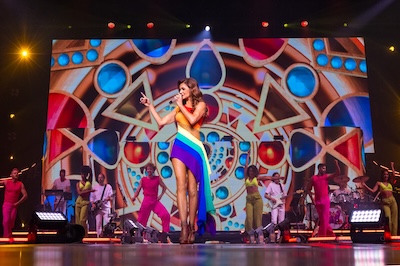 Andrea Berg auf der Bühne mit buntem Kleid, buntem und farbenprächtigem Hintergrund und Backgroundsänger:innen