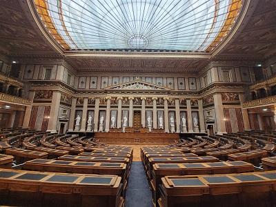 Historischer Sitzungssaal mit Glasdach, Statuen, Malereien und halbrunden Sitzreihen bei der Führung im Parlament