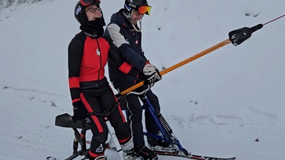 Jolly Schwarz und Julian Hager lachen während sie mit dem Skibob Schlepplift fahren.