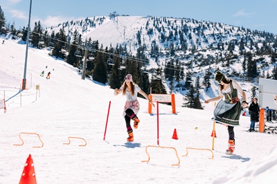 Mödels im Dirndl bei einem Geschicklichkeitsspiel beim Trachtengwand Skitag am Hochkar mit Piste im Hintergrund