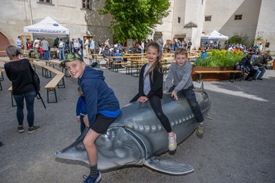 Drei Kinder sitzen auf einem Fischmodell im Hof beim Familienfest im Schloss Orth.